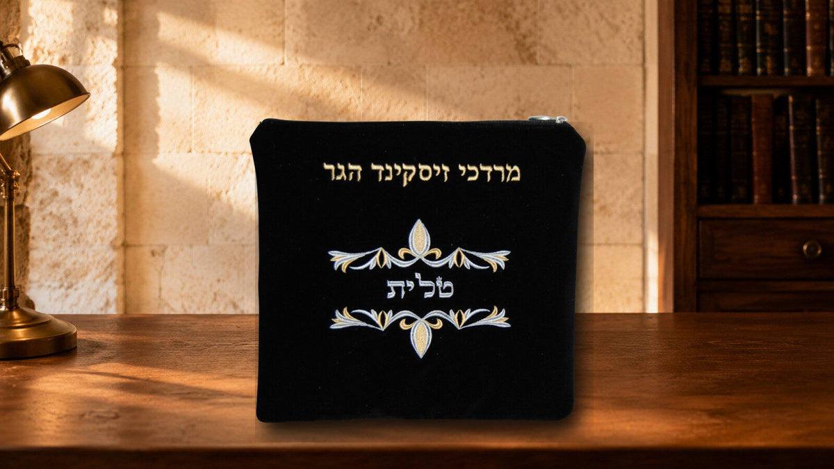Black velvet tallis bag with gold and silver embroidery displayed on a warm walnut desk