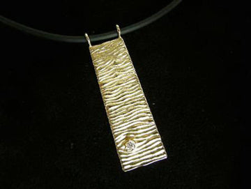 Long rectangular gold pendant with rippled wave texture and one diamond, on black cord