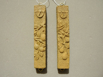 Pair of sand-colored stone mezuzah cases with pomegranate relief and shin on grey backdrop