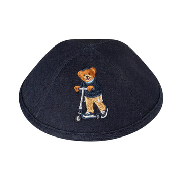 Navy denim boys kippah embroidered with a Dov Bear riding a silver kick scooter, wearing a navy sweater and light blue scarf