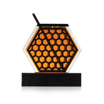 Hexagonal honey dish filled with honey, its black laser-cut honeycomb face front on, seated on the removable base