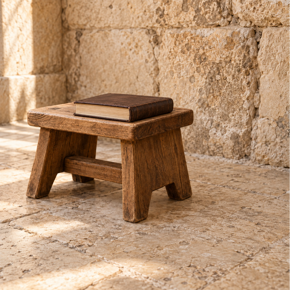 Closed prayer book resting on a low wooden stool beside a Jerusalem stone wall.