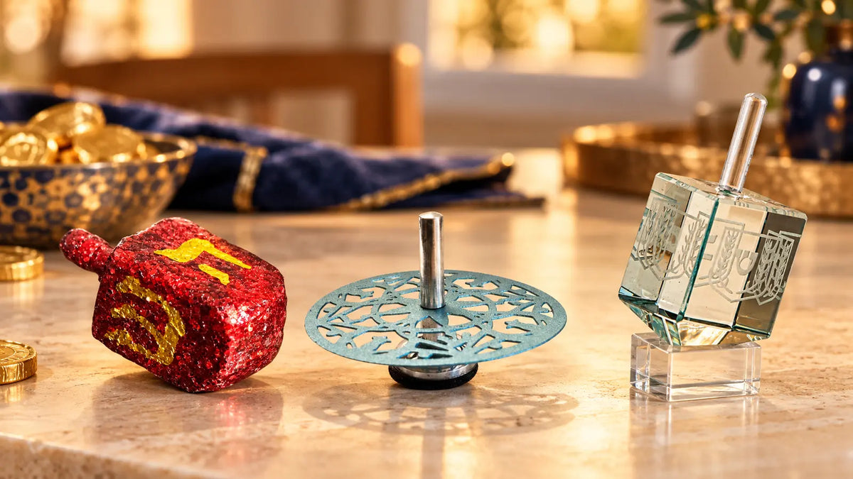 A red glitter wood dreidel, light blue metal dreidel and pale green glass dreidel on a warm Chanukah table