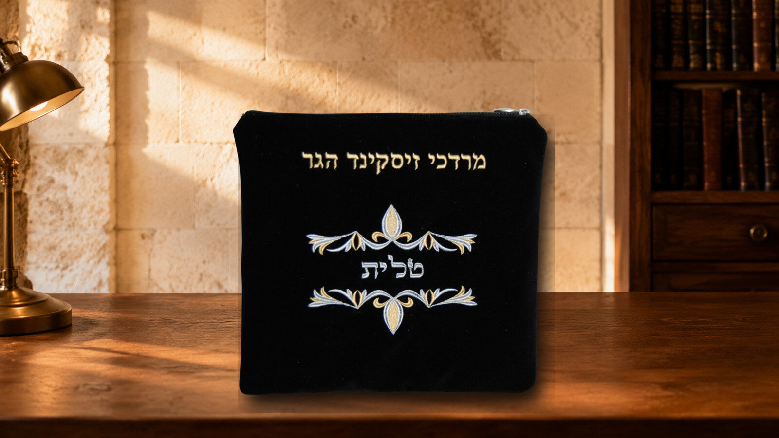Black velvet tallis bag with gold and silver embroidery displayed on a warm walnut desk