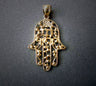 Lacy beaded gold filigree hamsa with a Hebrew letter at the center of the palm, on grey