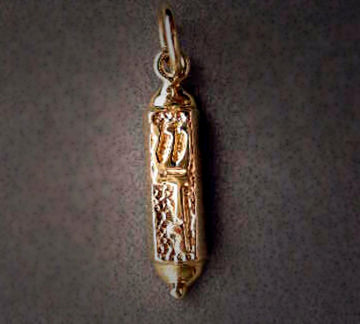 Petite gold mezuzah charm with raised tablet-like motif over a stippled body, on grey