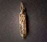 Petite gold mezuzah charm with raised tablet-like motif over a stippled body, on grey