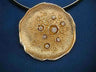 Textured gold disk pendant with bezel-set diamonds among raised circles, on a dark cord