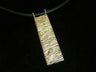 Long rectangular gold pendant with rippled wave texture and one diamond, on black cord