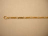 Close view of a gold Figaro chain with three short links between each long link