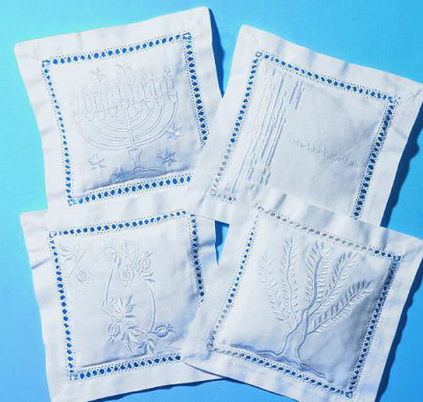 Four white hemstitched sachets embroidered with menorah, Shabbat, branch and tree designs on a blue backdrop
