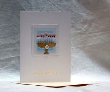 White Hanukkah card with a raised gold-tone menorah and pink flames on a light blue square panel