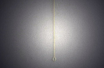 Very fine gold rolo chain suspended vertically with a small ring clasp at the end
