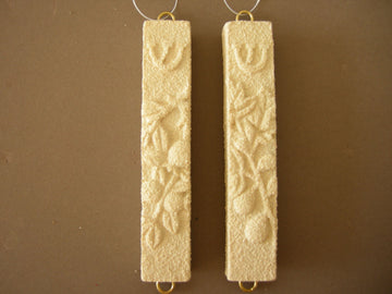 Pair of ivory stone mezuzah cases with raised pomegranates and shin, gold loops, on brown