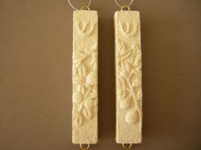 Pair of ivory stone mezuzah cases with raised pomegranates and shin, gold loops, on brown