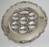 Round silver plated Seder plate with six Hebrew-labeled wells and a scrolled decorative rim