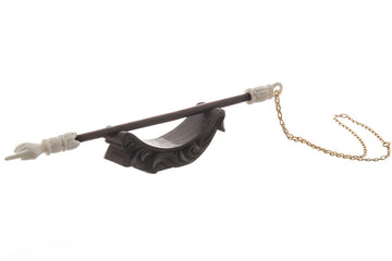 Two-tone carved yad with white pointing hand and dark shaft resting on a dark carved stand, gold-tone chain attached