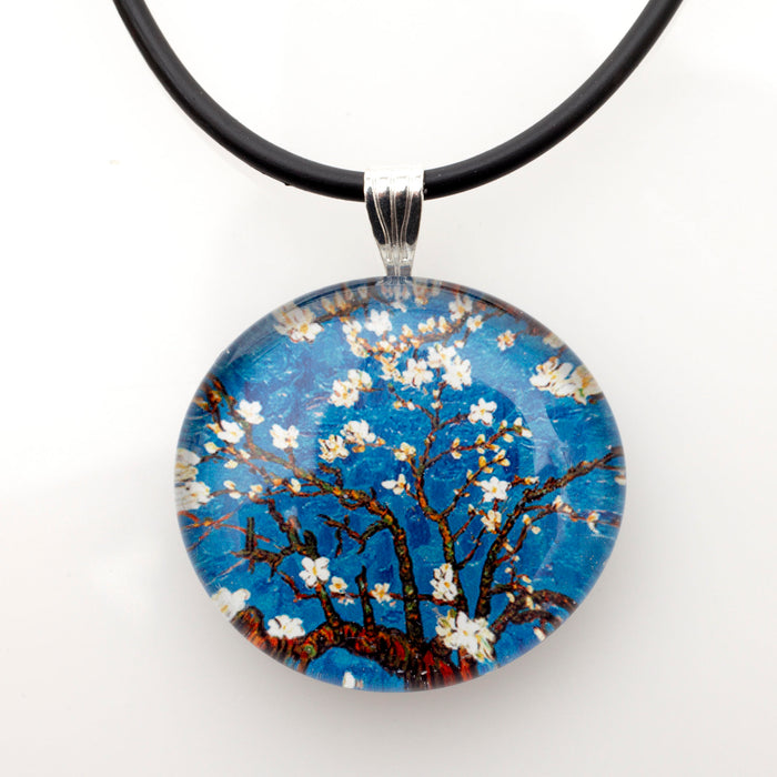 Round glass pendant showing white blossoms on dark branches against blue, on a black cord
