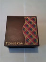 Top view of dark wood tzedakah box with red, blue and gold plaid straw wave and gold Tzedakah lettering