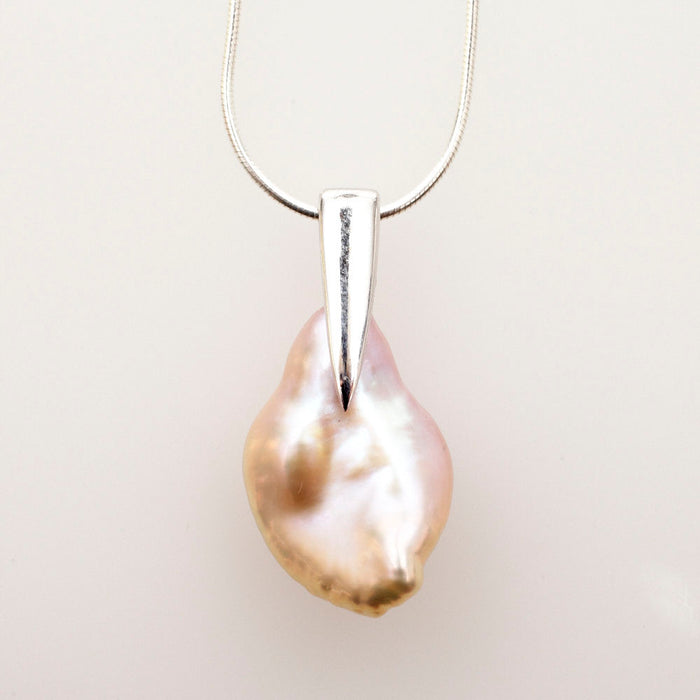 Irregular peach keshi pearl hanging from a tapered sterling silver bail on a snake chain