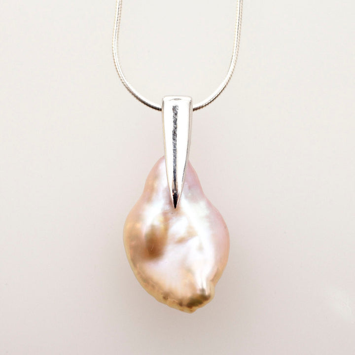 Irregular peach keshi pearl hanging from a tapered sterling silver bail on a snake chain