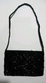 Black jet beaded shoulder bag with a long beaded strap, hanging against a white wall