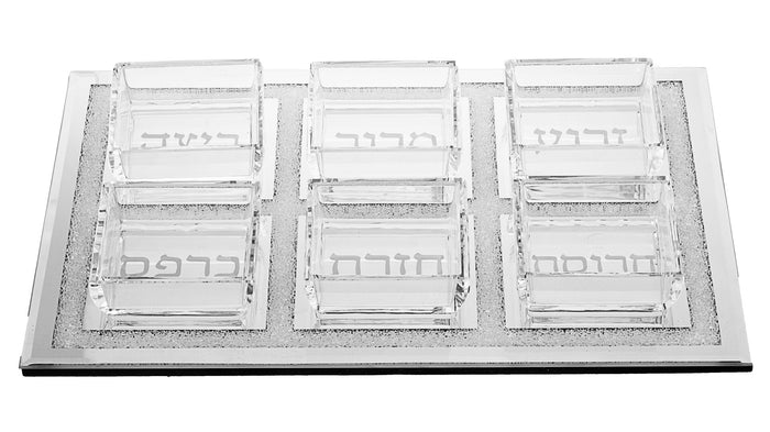 Rectangular glass Seder plate holding six square glass cups labeled in Hebrew, with sparkling border