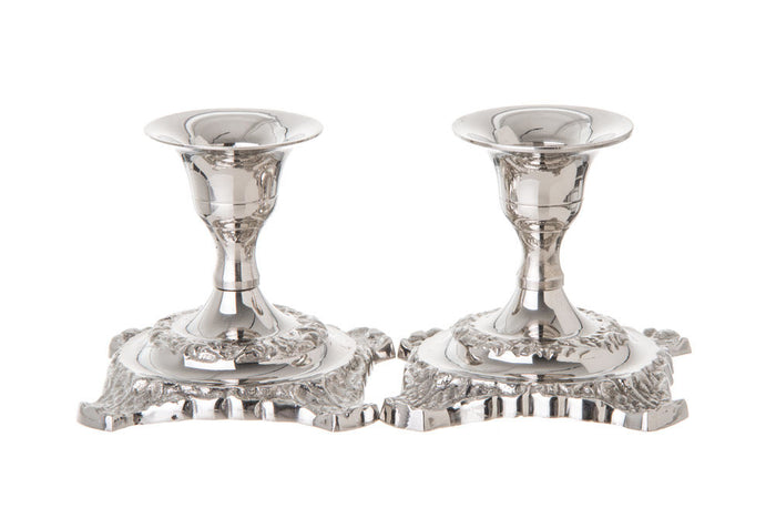 Two short polished stainless steel candlesticks with ornate scrolled square bases