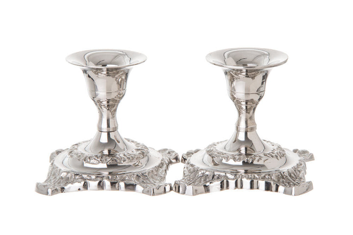 Two short polished stainless steel candlesticks with ornate scrolled square bases