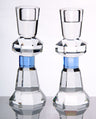 Two faceted clear crystal candlesticks with a blue band below the collar, reflected on a glossy surface