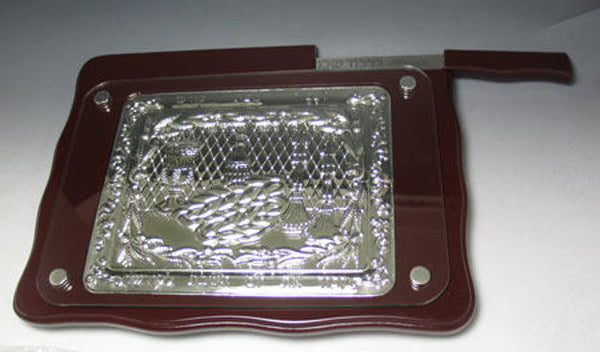 Rectangular mahogany-tone challah board with embossed silver-tone panel under clear cover, knife on top