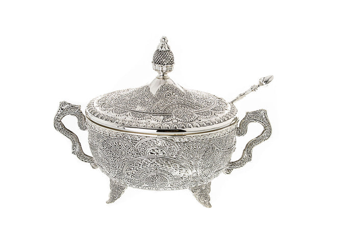 Silver-tone filigree honey dish with domed lid, two curved handles, small feet and a slender spoon