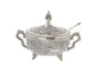 Silver-tone filigree honey dish with domed lid, two curved handles, small feet and a slender spoon