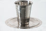 Tumbler-style hammered stainless steel Kiddush cup on a smooth round tray