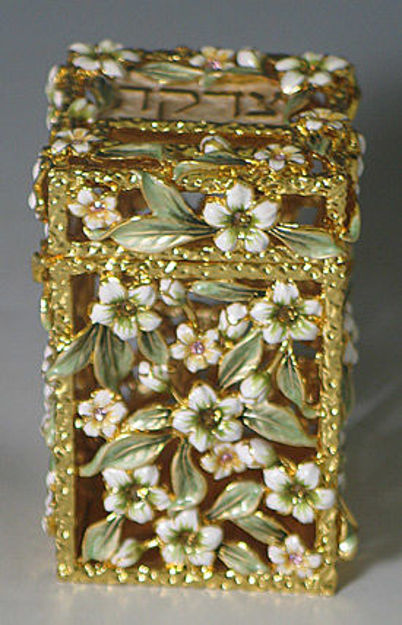 Gold-tone jeweled tzedakah box covered in white flowers with green leaves and small stones