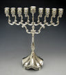 Silver plated menorah with looped scroll arms, raised center shamash and fluted flared base on grey