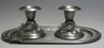 Two short pewter candlesticks with grape leaf clusters standing on an oval pewter tray