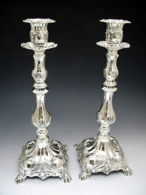 Pair of tall ornate silver plated candlesticks with scroll relief and square footed bases on grey