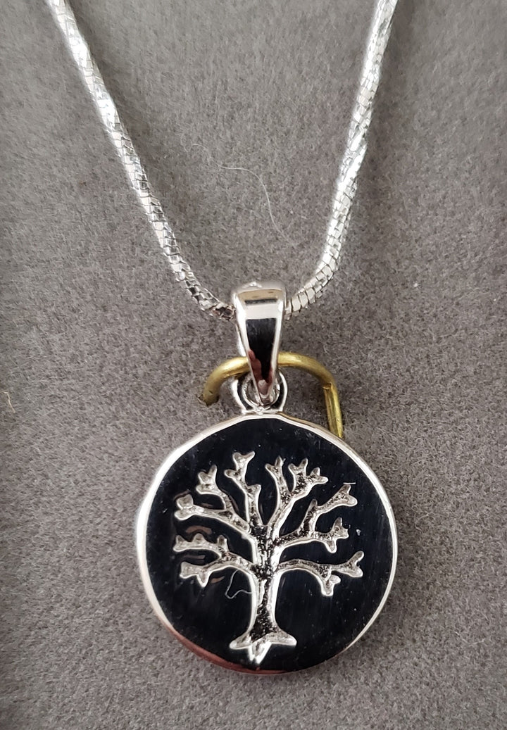 Petite round medallion with a raised silver Tree of Life on a black field, snake chain, gray backdrop