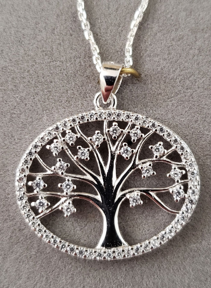 Oval Tree of Life pendant with CZ-set leaves and stone-lined rim hanging from a fine chain on grey