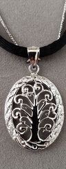 Oval Balinese-style Tree of Life pendant with dark backing, worn on black silk cord beside a silver chain