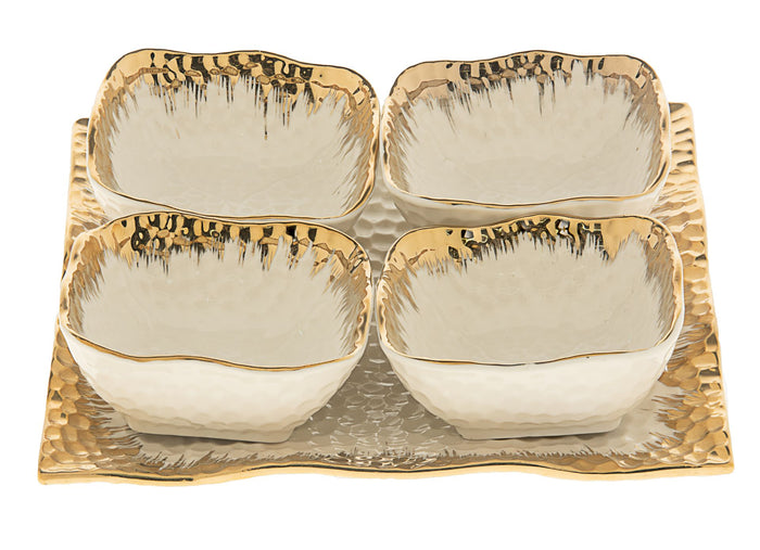 Four white porcelain square dishes with brushed gold rims on a gold hammered square tray