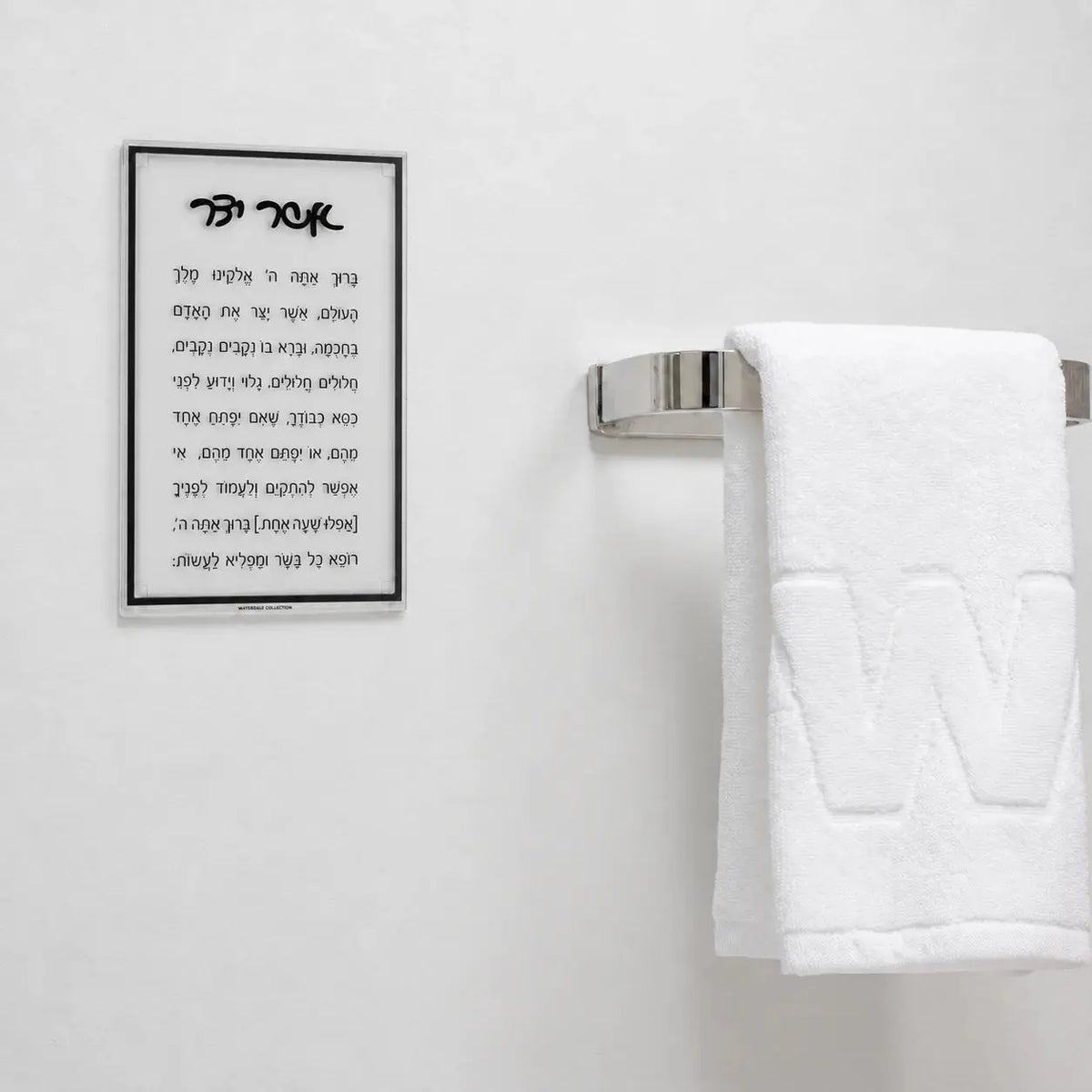 Classic Black Asher Yatzar plaque mounted on a white wall beside a towel bar, showing the 5 x 8 in size in a vanity setting