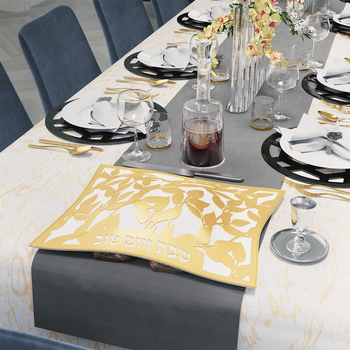 Gold leaf challah cover on a grey runner at a set Shabbos table with wine and flowers