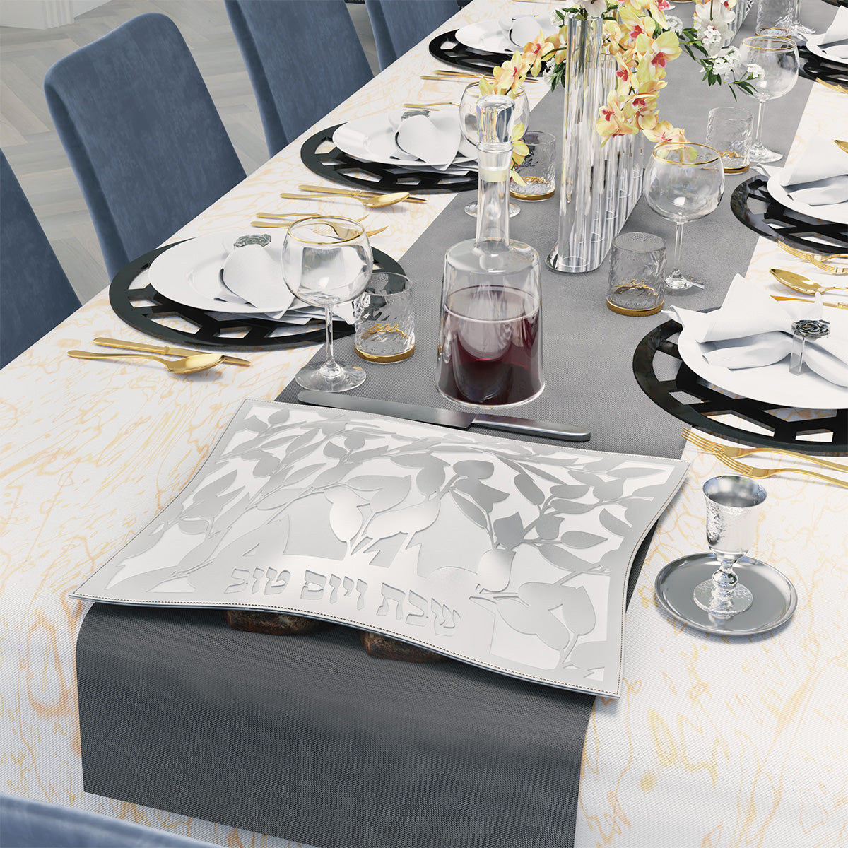 Silver leaf challah cover on the Shabbos table beside a kiddush cup on its plate