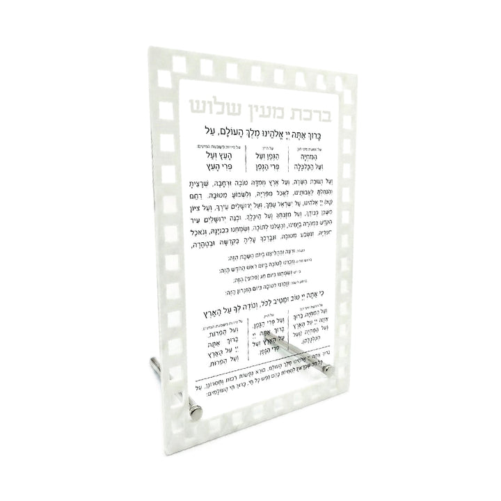 Al Hamichya table card with a white marble checked border framing the black Bracha Me'ein Shalosh text, on clear stand posts