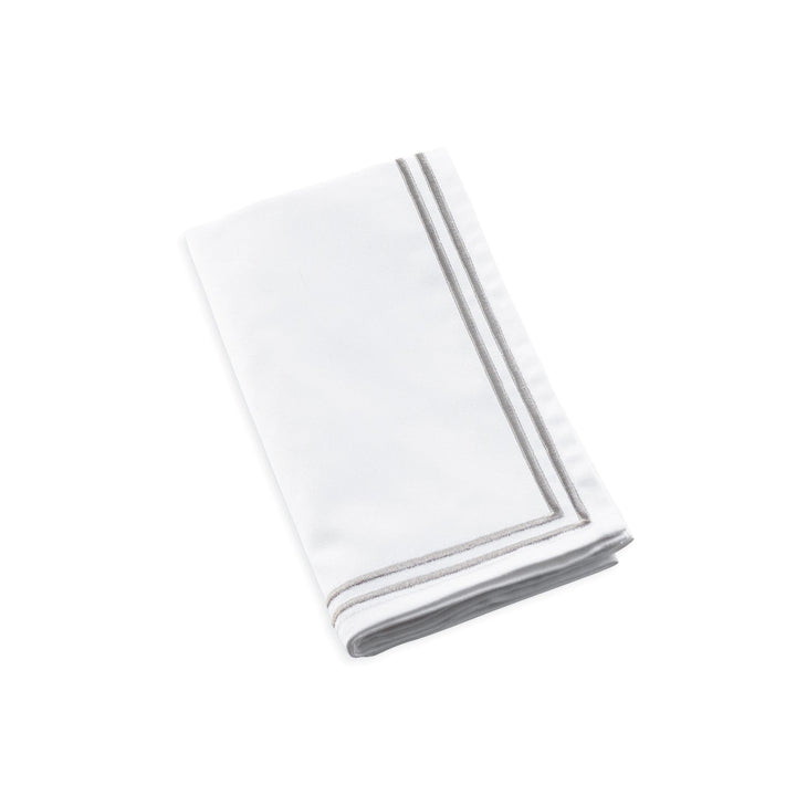 White cloth napkin folded to show two parallel silver-grey stripes stitched along its hem