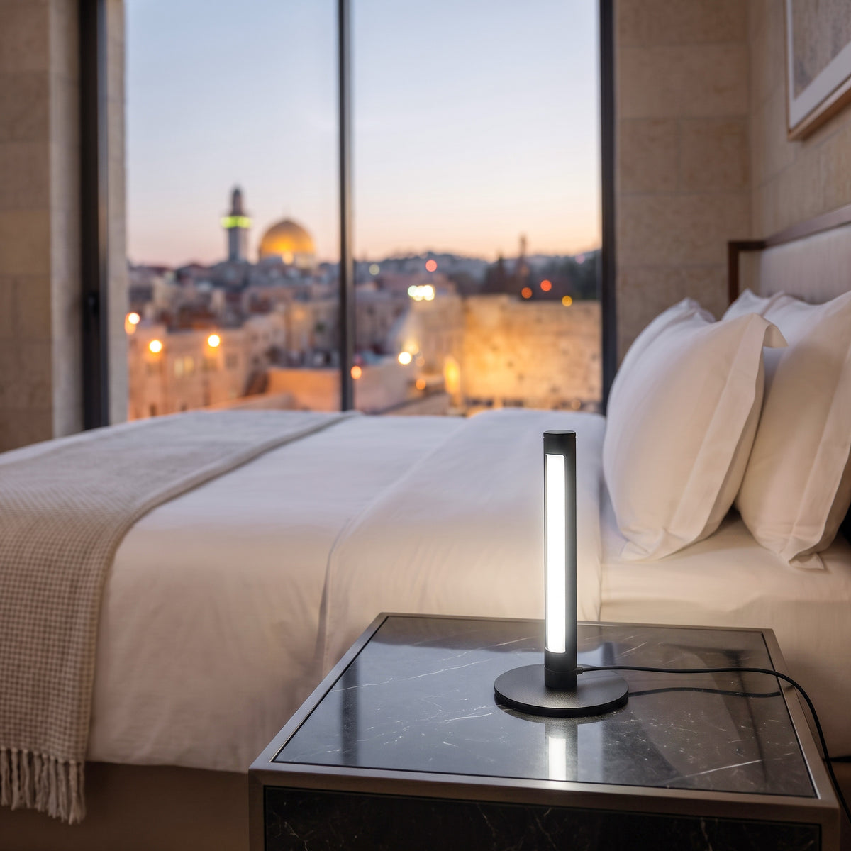 Black Shabbostick Mini lit on a hotel nightstand by the bed