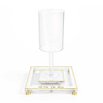 Tall clear lucite Kos Shel Eliyahu standing empty on its gold-rimmed marble tray