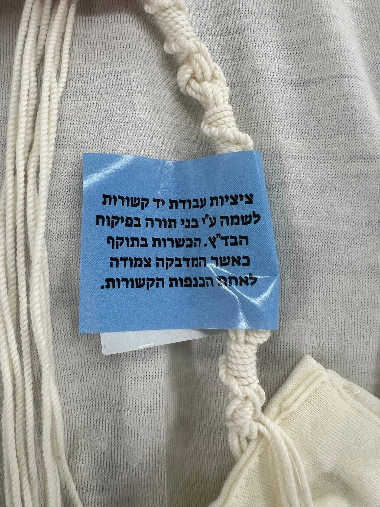 Wool tzitzit corner close-up with hand-tied strings and supervision tag